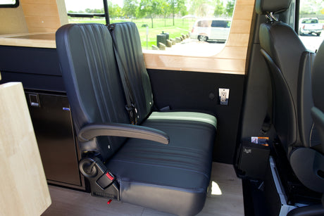 This RV rental interior shows comfortable black passenger seating, fridge, power outlets, and wood trim for your adventure van.