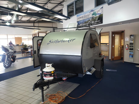 A Bushwhacker travel trailer, perfect for RV rental adventures, displayed in an RV dealership showroom.
