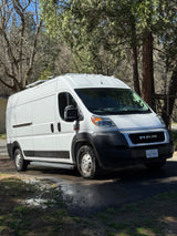 White Ram ProMaster camper van with solar panels, a great RV rental option, parked under sunny trees.