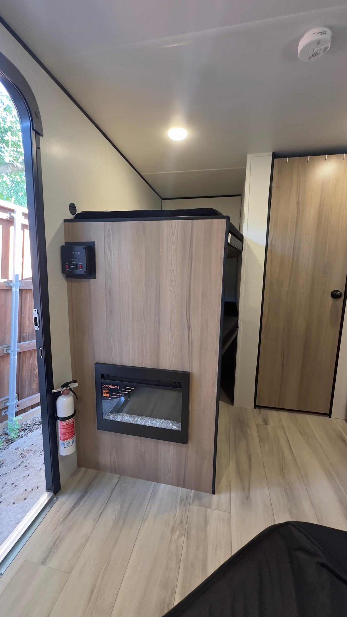 Modern RV rental interior with a fireplace, control panel, bunk bed, wood flooring, and fire extinguisher near the entry door.