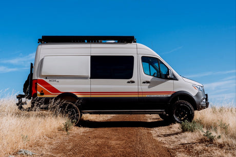 Storyteller Overland MODE 4x4 camper van, perfect for rv rental adventures, on a dirt path under a clear blue sky.