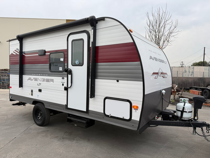 A compact white, red, and gray Primetime Avenger LT travel trailer, ideal for an rv rental, parked outdoors. — photo 1