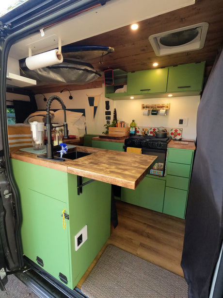 This rv rental shows a compact, well-equipped camper van kitchen with green cabinets, a sink, and stove, perfect for mobile living.