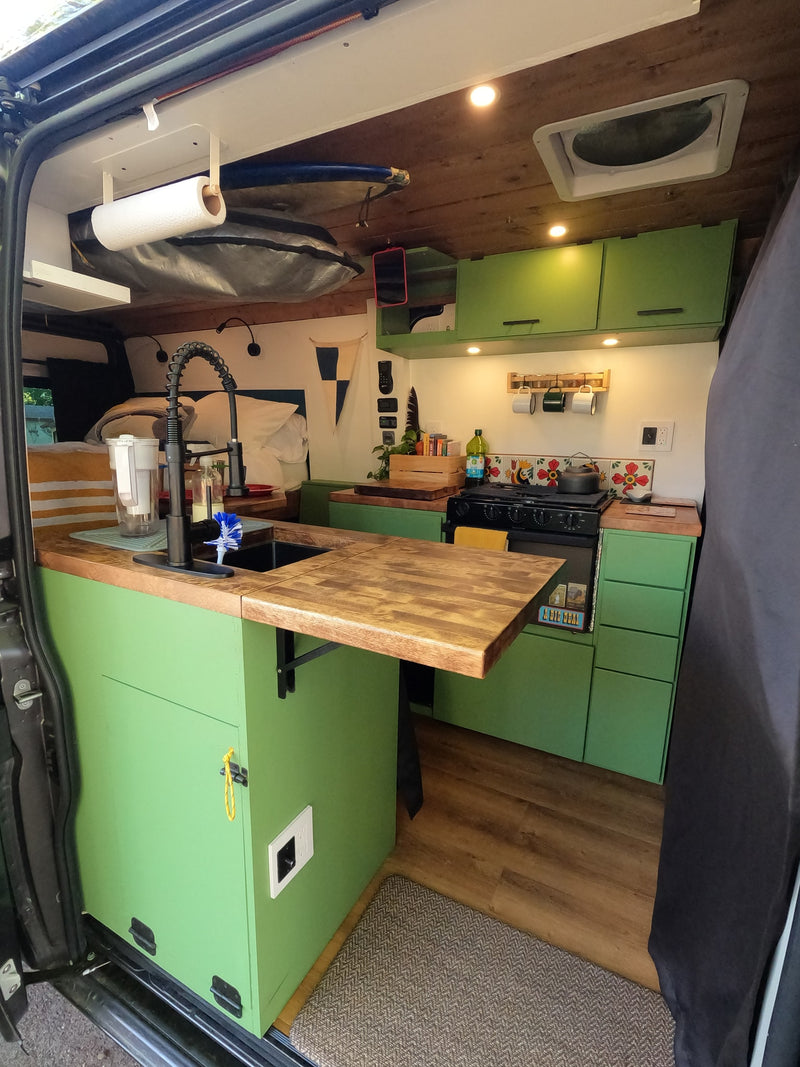 This rv rental shows a compact, well-equipped camper van kitchen with green cabinets, a sink, and stove, perfect for mobile living. — photo 2