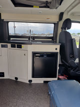 Rv rental interior: Compact kitchenette with sink, Dometic fridge, induction cooktop, control panel, and passenger seating.