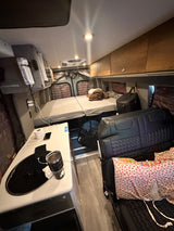 Cozy RV rental interior shows a compact bed, kitchen counter with sink, and a seating area for comfortable travel.