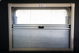 Inside an RV rental: a window with pleated blinds, partially open for light. An "EXIT" sign is above.