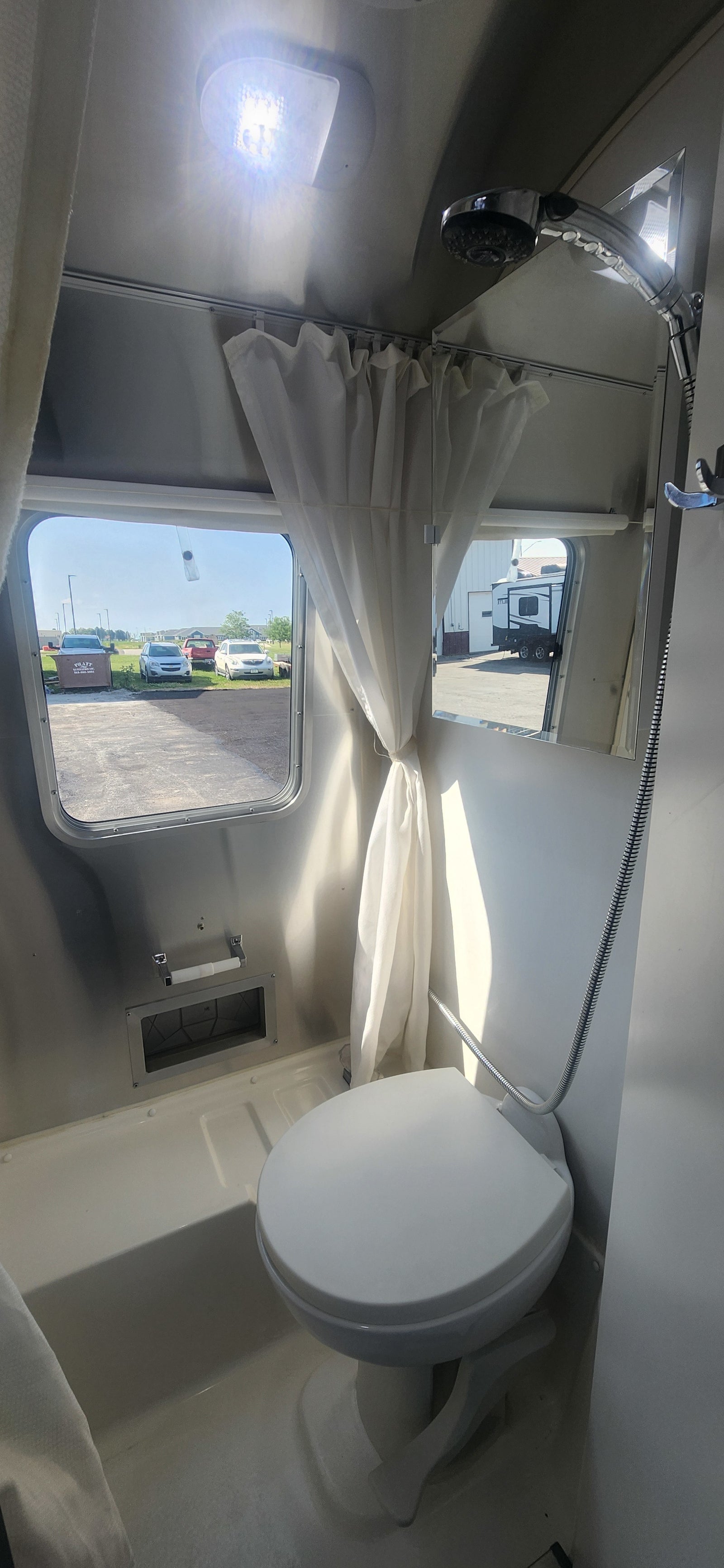 Interior of an RV rental bathroom with a toilet, shower, windows, and bright ceiling light, showing compact design.