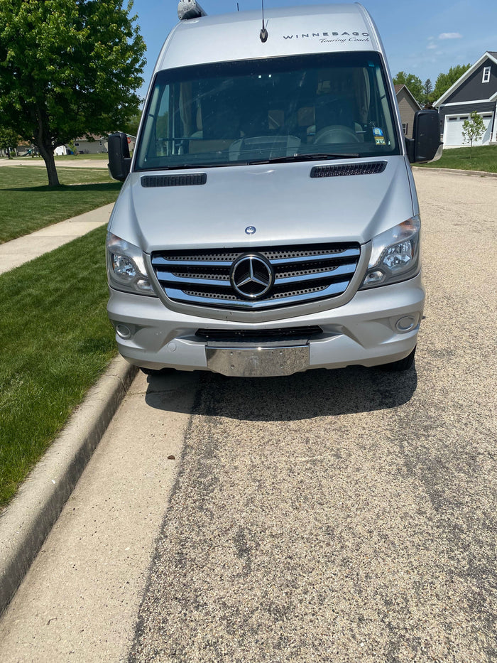This silver Winnebago Touring Coach rv rental is parked on a sunny suburban street, ready for your next road trip adventure.