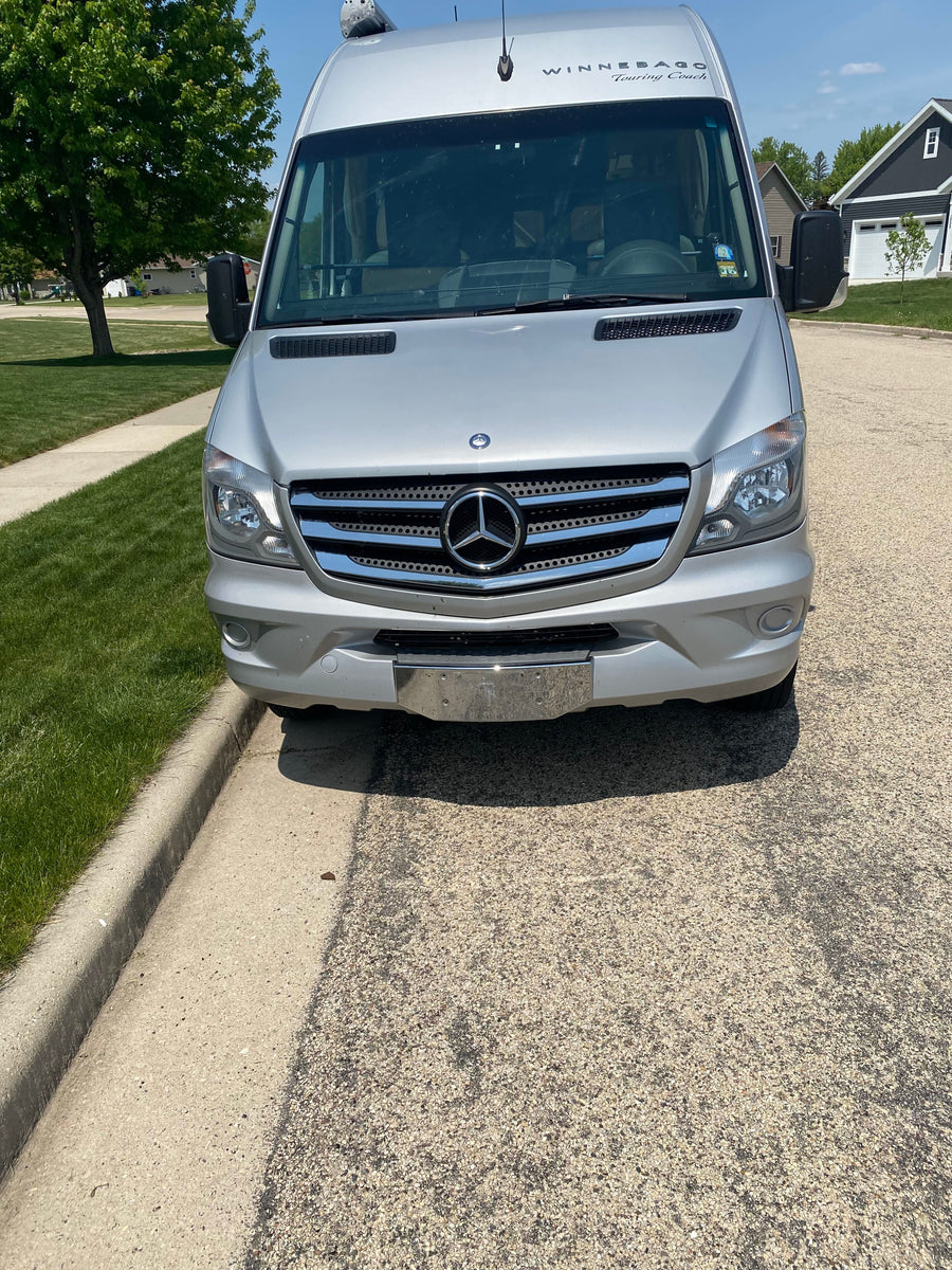 This silver Winnebago Touring Coach rv rental is parked on a sunny suburban street, ready for your next road trip adventure.