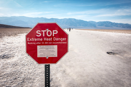 A red sign warns of "Extreme Heat Danger" in a vast desert. Walking after 10 AM is not recommended. An rv rental allows safe exploration.