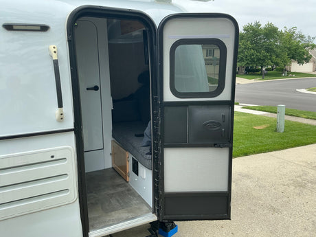 Inside a compact RV rental, showing the open door, cozy interior, and outdoor view from the entrance.