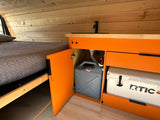 Interior of an RV rental: features a cozy bed, compact kitchen with a sink, water tank, and an RTIC cooler.