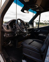 Driver's cockpit of an accessible Mercedes-Benz van for rv rental, featuring hand controls, adapted pedals, and black leather seat.