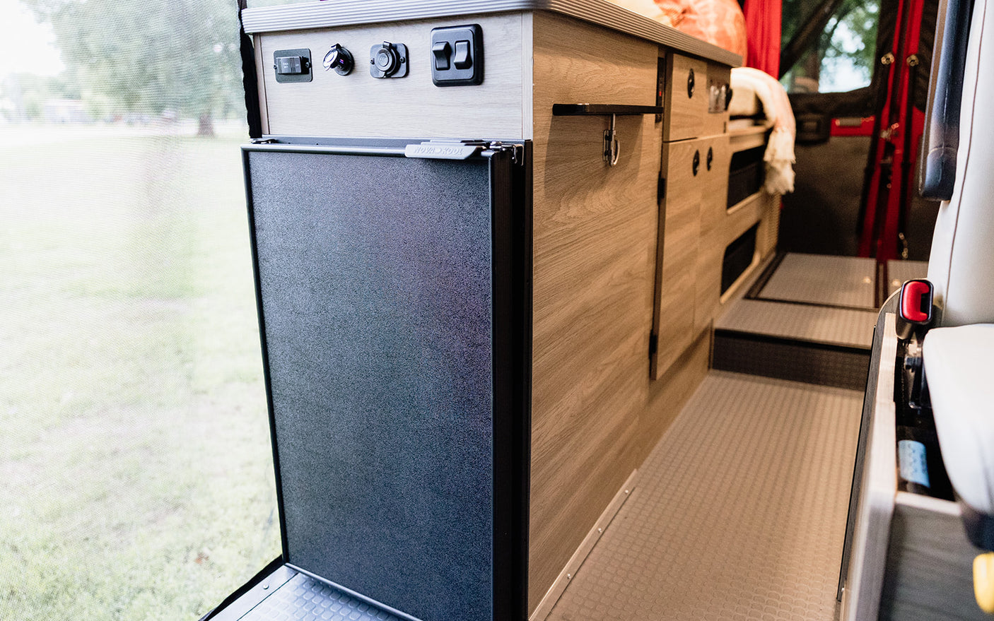 RV rental: Inside a camper van with a Nova Kool refrigerator, control panel, and wood storage cabinets.