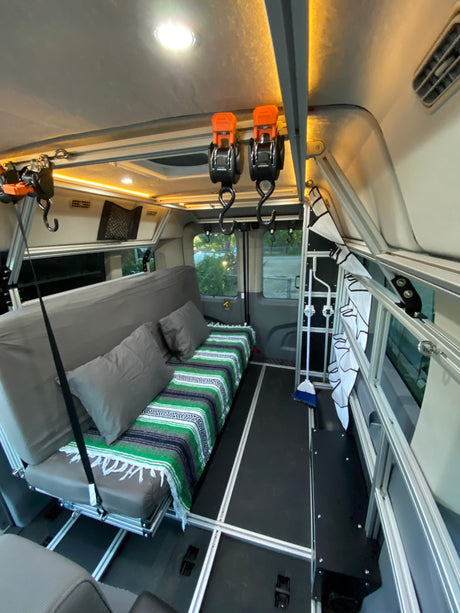 Inside an rv rental camper van: sofa bed with blanket, modular aluminum frame, bright lighting, and overhead hooks.