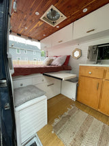 Explore this modern RV rental camper van interior. Features a cozy bed, pull-out table, kitchen, storage, and wood ceiling.