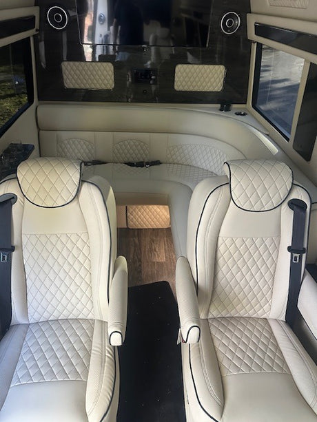 Luxury RV rental interior with white quilted leather captain seats & a spacious curved sofa, designed for premium travel comfort.