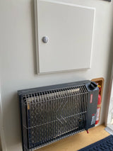 Compact Olympian Wave 6 propane heater and fire extinguisher inside an rv rental, with an access panel above.
