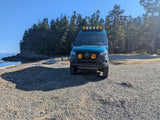 Custom teal Sprinter van, perfect for an RV rental adventure, parked on a gravel beach near forested ocean cliffs.