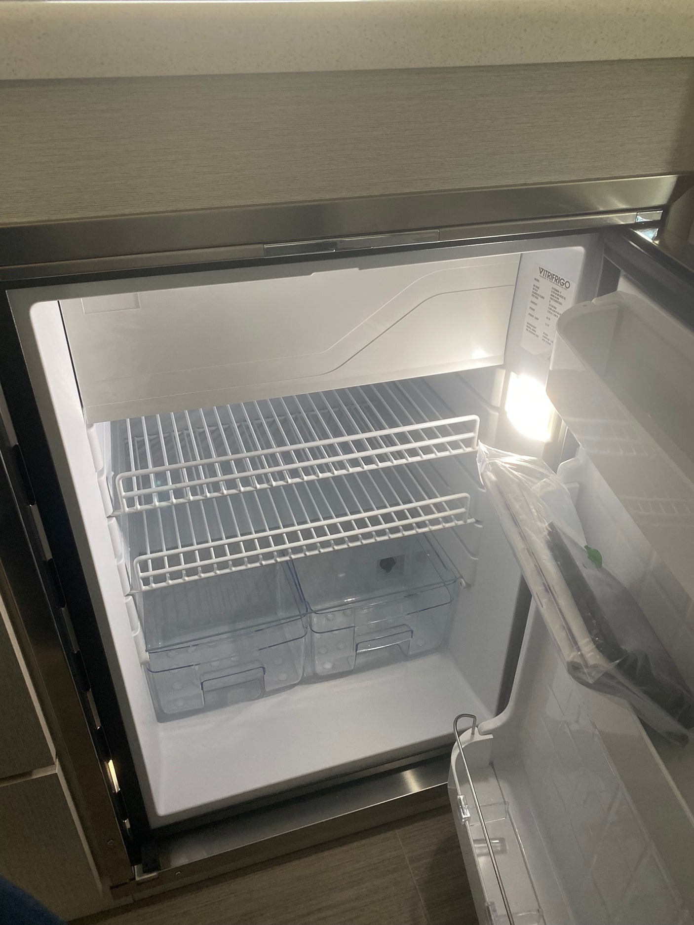 This rv rental's VITRIFRIGO refrigerator is open and empty, revealing its interior shelves and crisper drawers.