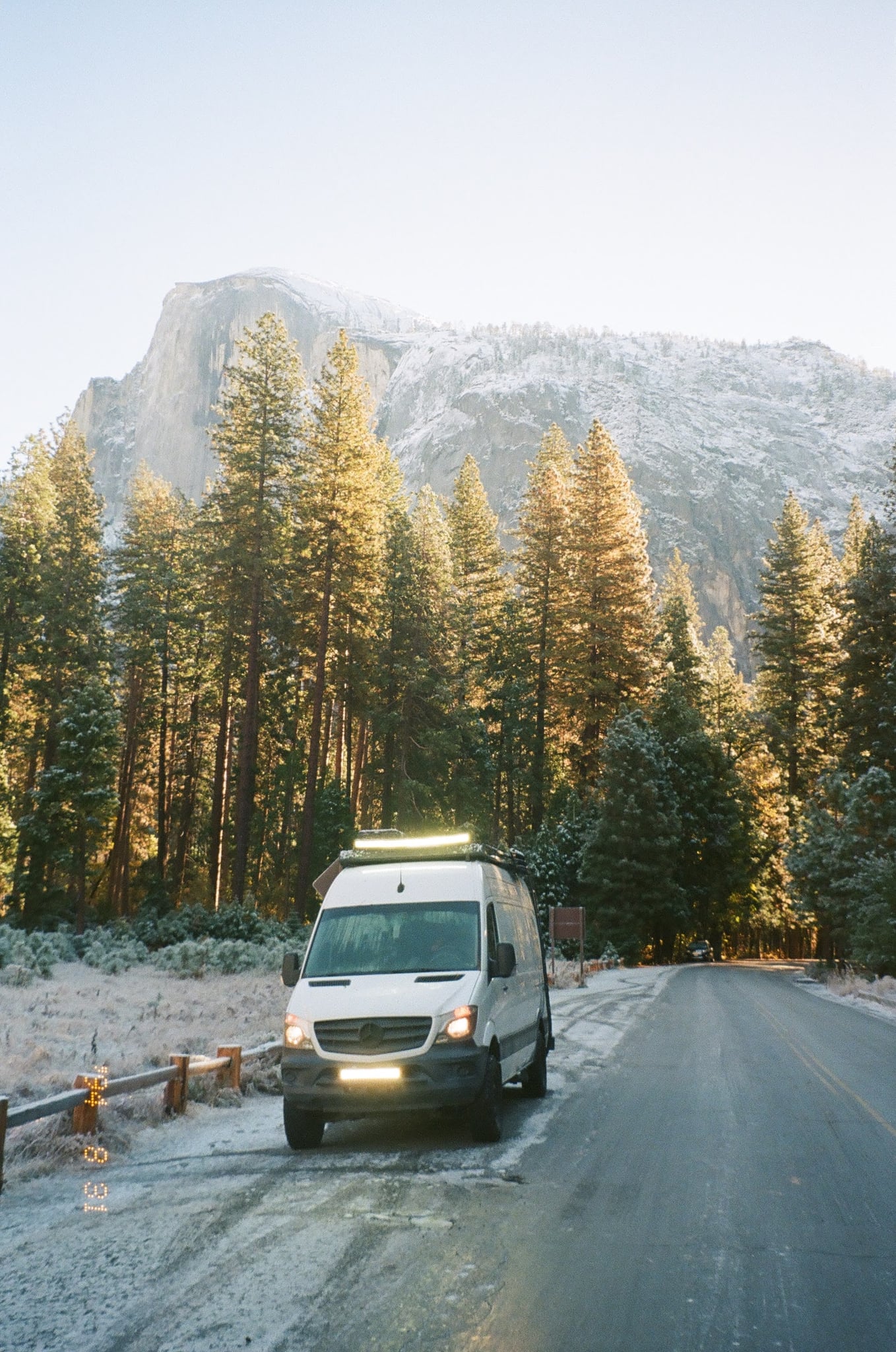  parked on a dirt road in a desert with rocky hills and snowy mountains.|A white RV rental camper van is parked on a dirt path at a dramatic cliff edge overlooking a vast sandy beach and ocean.|Customized white Sprinter RV rental with roof rack & ladder — photo 20