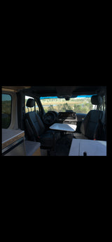 Spacious RV rental interior featuring swiveled front seats, a dining/workspace table, and a view of nature.