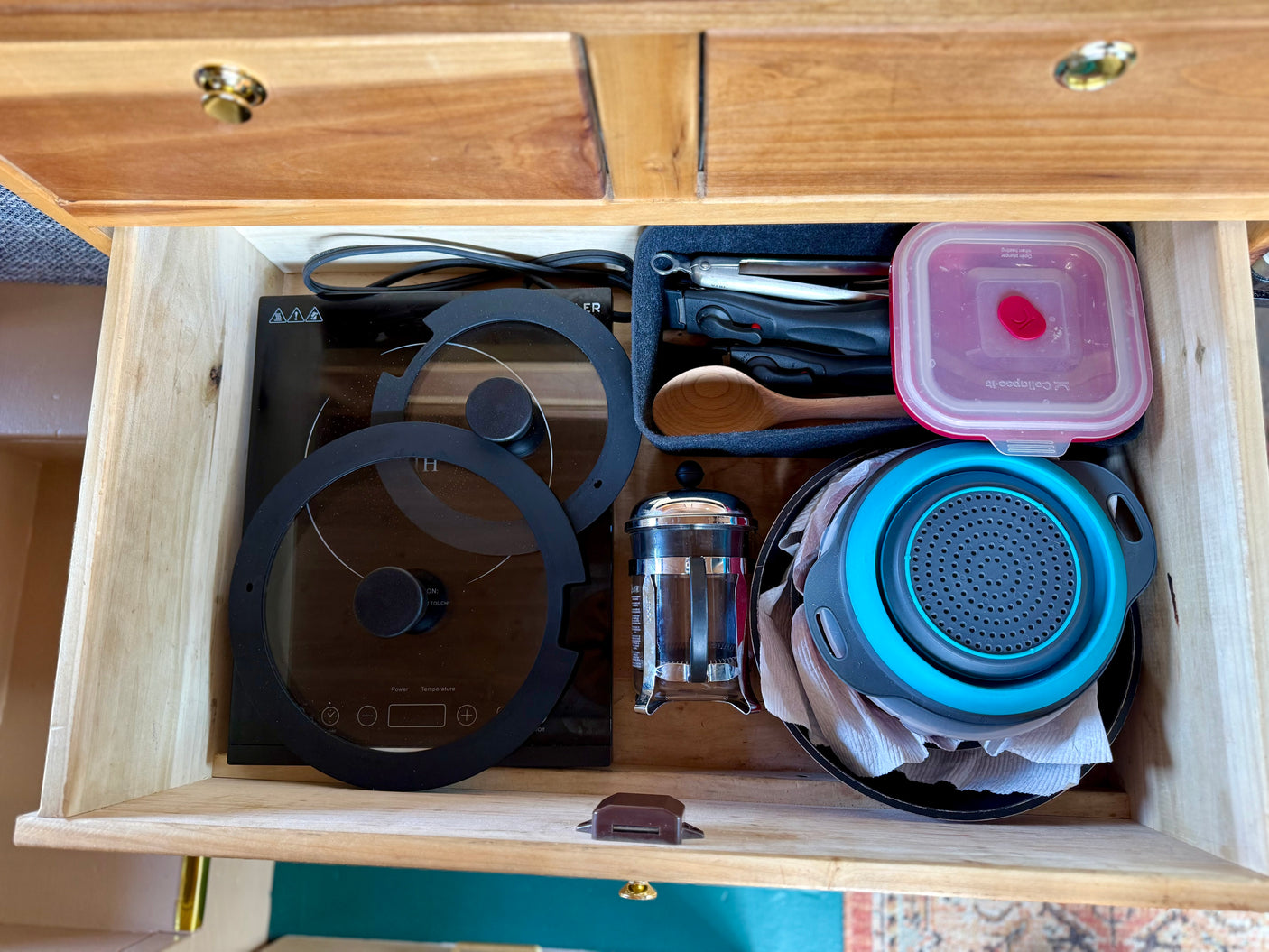 Compact RV rental kitchen drawer with an induction cooktop, French press, and collapsible kitchenware for efficient travel.