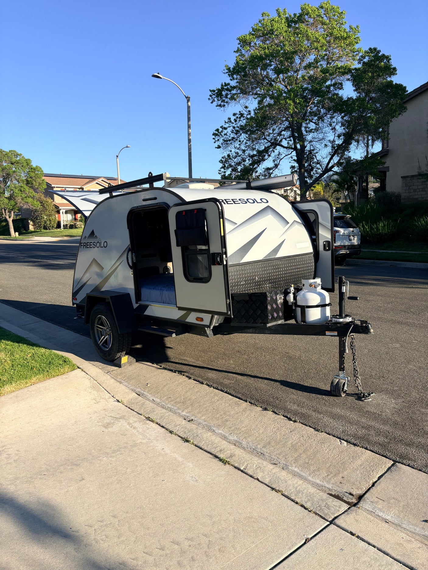 This compact FreeSolo teardrop travel trailer RV rental is parked on a residential street, doors open, ready for its next adventure.