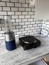 Compact rv rental kitchenette with a personal blender, portable hot plate, and paper towels on a modern tiled counter.