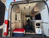 The organized interior of an RV rental camper van from the back, featuring a convertible bed, storage, and ceiling AC.