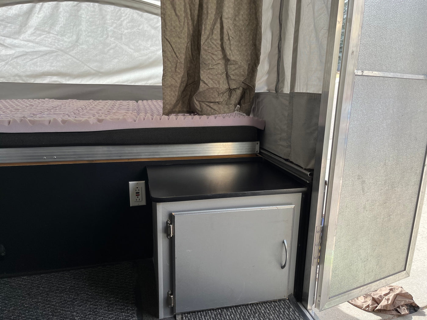 RV rental interior: cozy bed with egg-crate mattress, a cabinet, and an outlet in a pop-up camper. — photo 10