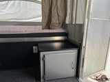 RV rental interior: cozy bed with egg-crate mattress, a cabinet, and an outlet in a pop-up camper.