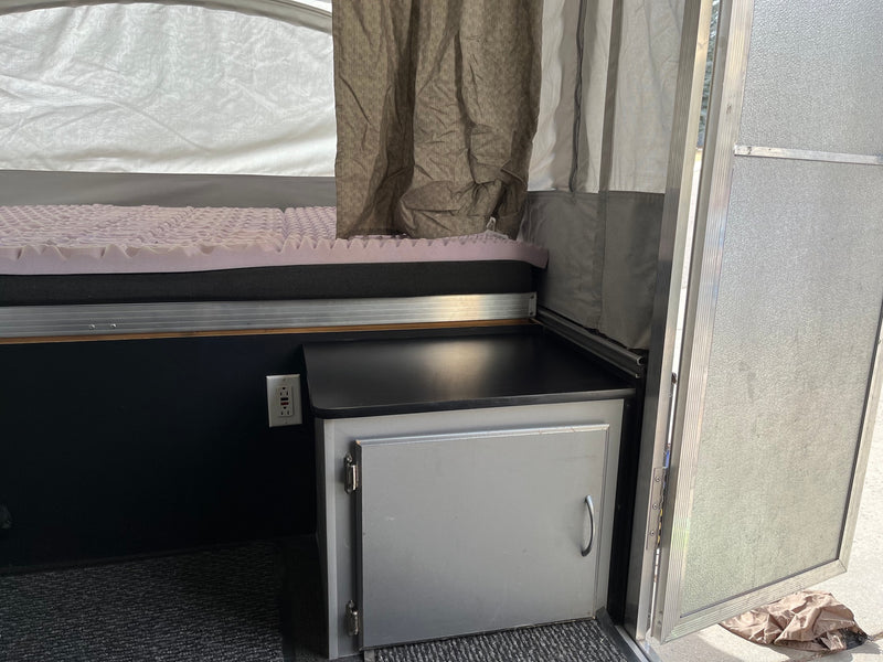 RV rental interior: cozy bed with egg-crate mattress, a cabinet, and an outlet in a pop-up camper. — photo 10