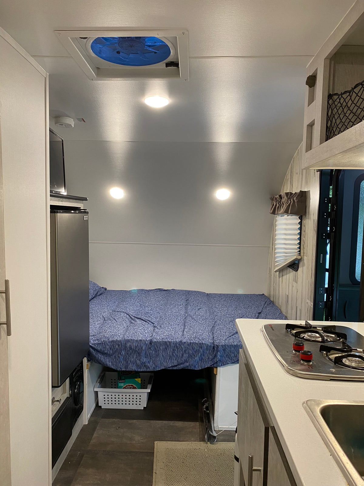 Compact RV rental interior showing bed, kitchen with stove/sink, fridge, and overhead fan. Ideal for road trips. — photo 3