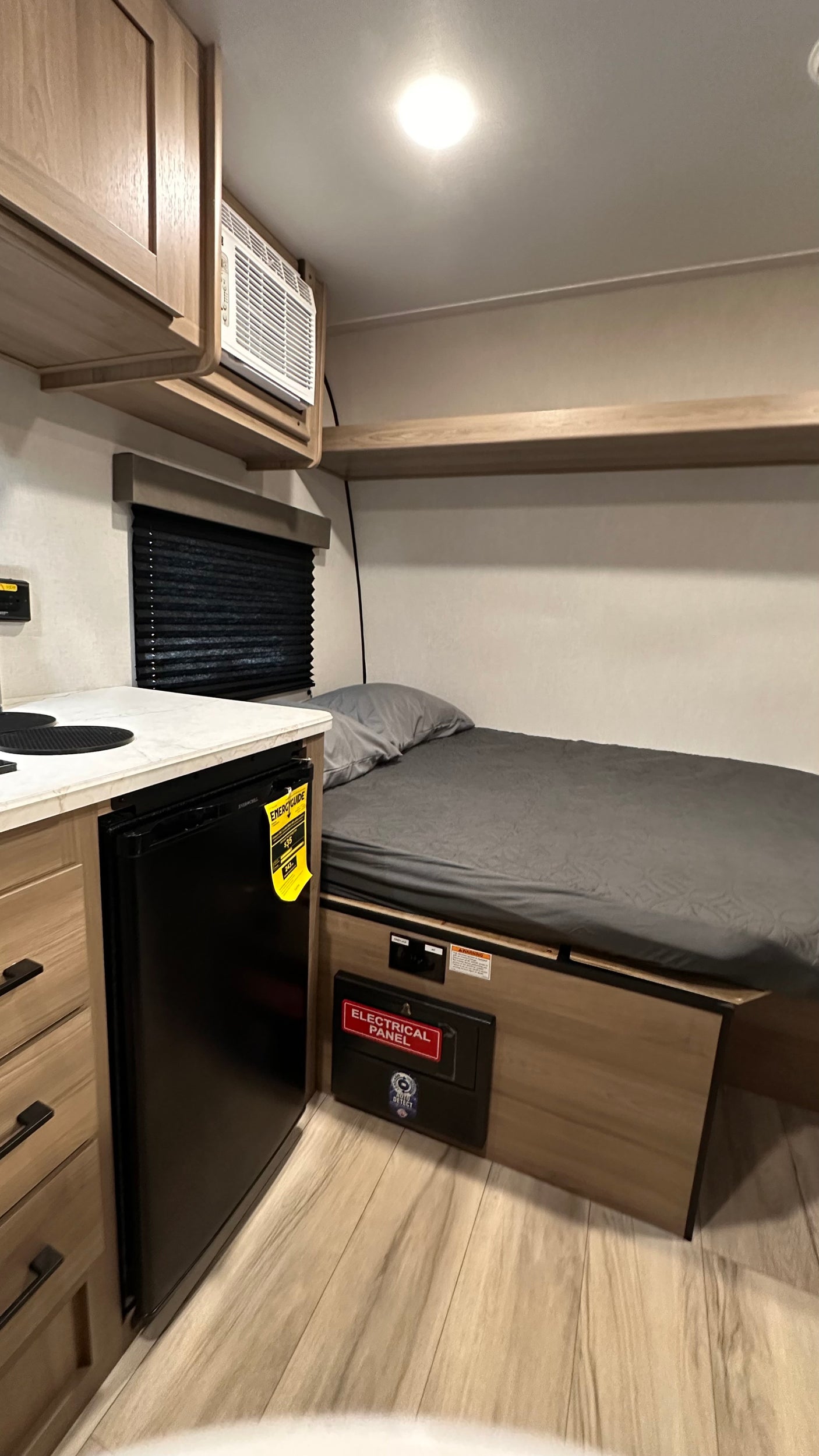 Compact RV rental interior: bed, mini-fridge, AC unit, and kitchen counter with cabinets. Ideal for a cozy adventure.