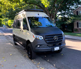 Custom two-tone Mercedes Sprinter camper van, perfect for RV rental adventures, parked under trees on a sunny street.