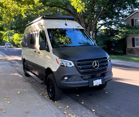 Custom two-tone Mercedes Sprinter camper van, perfect for RV rental adventures, parked under trees on a sunny street.