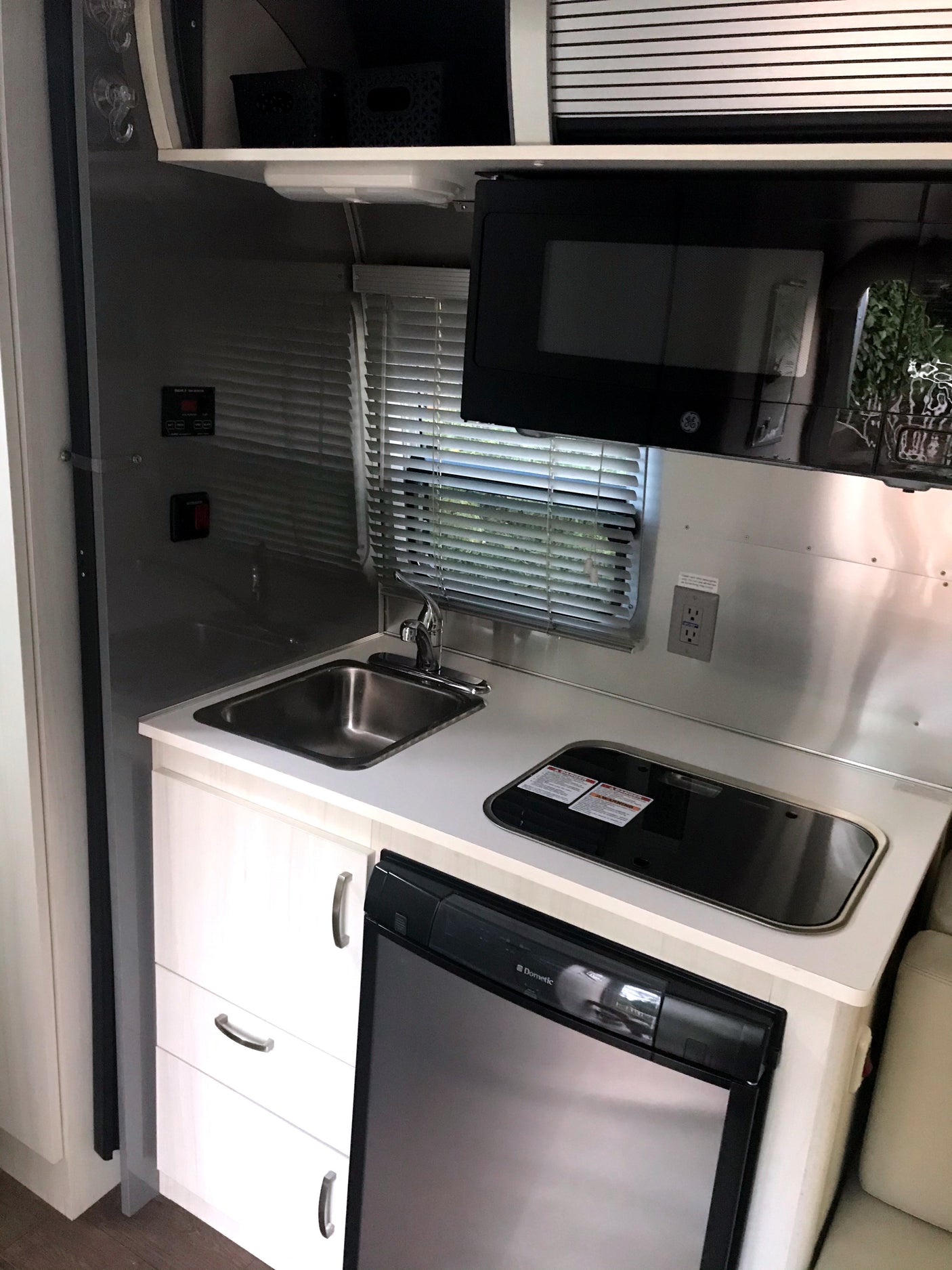 This rv rental offers a compact kitchen setup with a stainless steel sink, stovetop, Dometic fridge, and microwave.