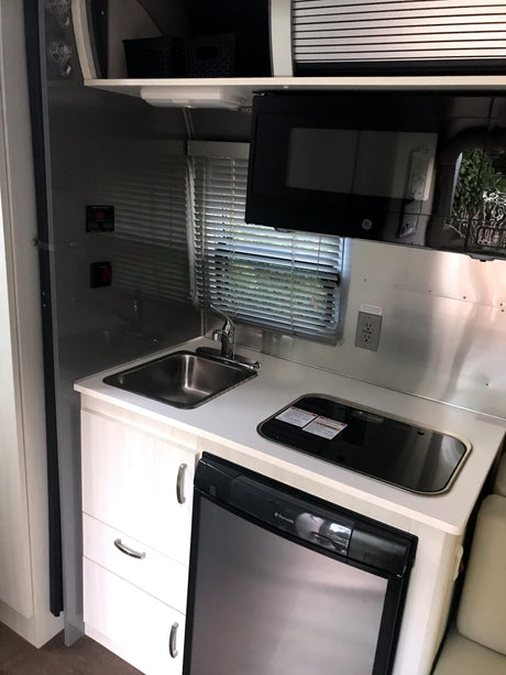 This rv rental offers a compact kitchen setup with a stainless steel sink, stovetop, Dometic fridge, and microwave.