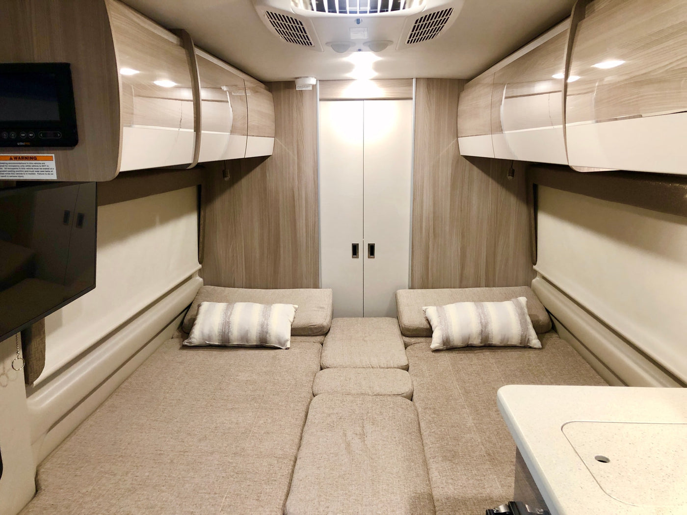 Spacious RV rental interior featuring convertible beds, ample overhead storage, TV, and a functional tabletop, ideal for comfortable road trips. — photo 8