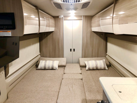 Spacious RV rental interior featuring convertible beds, ample overhead storage, TV, and a functional tabletop, ideal for comfortable road trips.