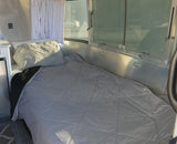 Bright RV rental interior: a comfy bed by panoramic windows, offering a glimpse of the passing road.
