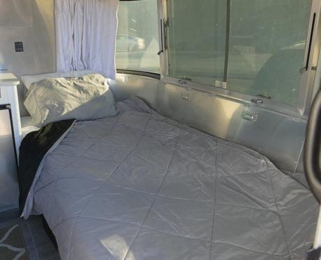 Bright RV rental interior: a comfy bed by panoramic windows, offering a glimpse of the passing road.