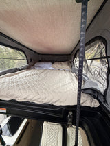 Cozy rv rental pop-top camper bed with quilted comforter & mesh windows offering outdoor views for a comfortable night.