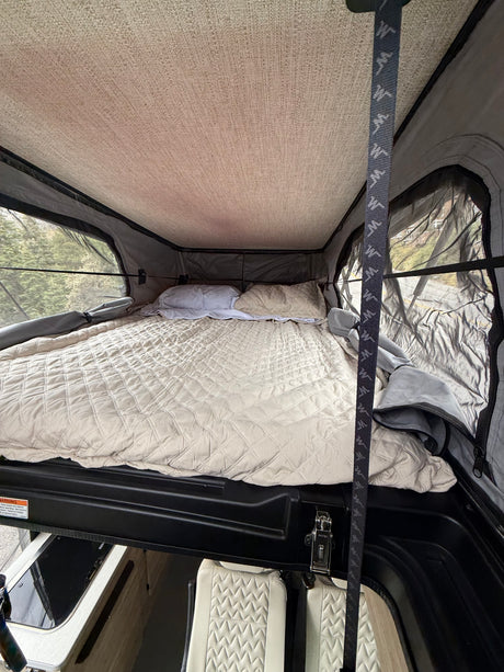 Cozy rv rental pop-top camper bed with quilted comforter & mesh windows offering outdoor views for a comfortable night.