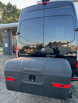 Rear view of a black Mercedes-Benz Sprinter van with a large, dark storage box mounted on the hitch. An RV rental option, ready for travel.