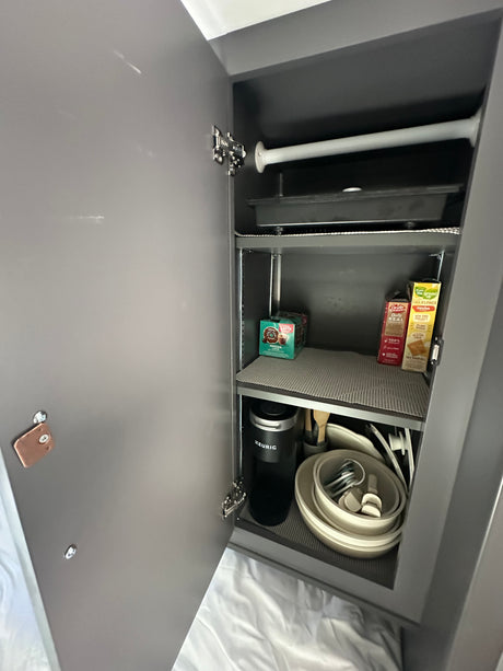 RV rental kitchen cabinet, neatly organized with a Keurig coffee maker, dishes, and snacks for travel convenience.