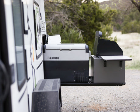 An RV rental's extended side compartment reveals a Dometic portable fridge and an outdoor grill station, ready for adventure.