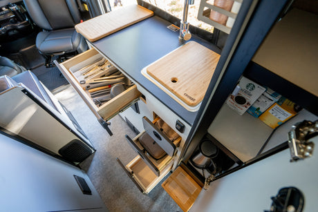Functional RV rental kitchen with open drawers revealing organized utensils, sink, and coffee supplies.